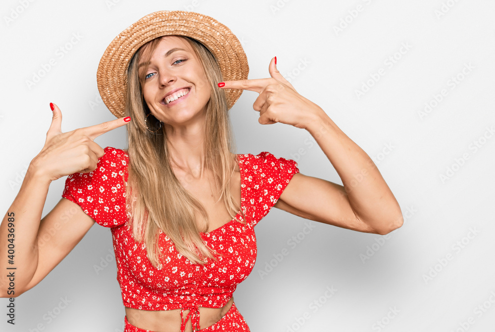 Beautiful caucasian woman wearing summer hat smiling cheerful showing and pointing with fingers teeth and mouth. dental health concept.
