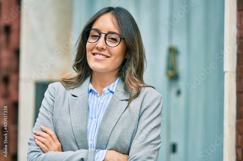 Obraz na plátně Young hispanic businesswoman with arms crossed smiling happy at the city