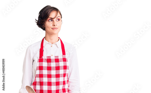 Beautiful young woman with short hair wearing professional cook apron smiling looking to the side and staring away thinking.