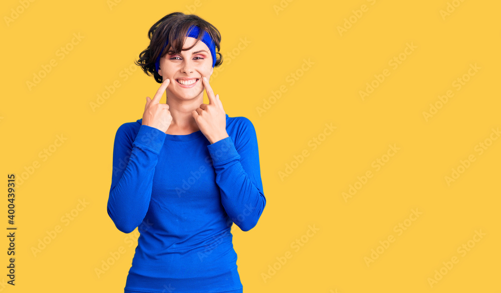 Beautiful young woman with short hair wearing training workout clothes smiling with open mouth, fingers pointing and forcing cheerful smile Beautiful young woman with short hair wearing training workout clothes smiling with open mouth, fingers pointing and forcing cheerful smile