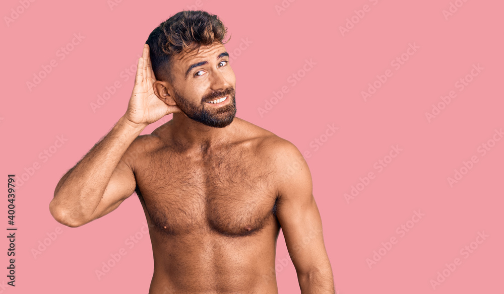 Young hispanic man wearing swimwear shirtless smiling with hand over ear listening an hearing to rumor or gossip. deafness concept.