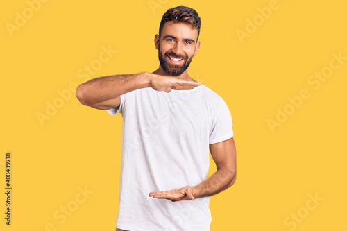 Young hispanic man wearing casual white tshirt gesturing with hands showing big and large size sign, measure symbol. smiling looking at the camera. measuring concept.