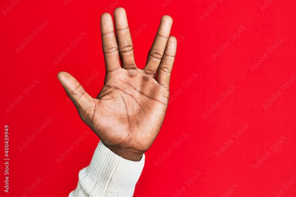 Arm and hand of african american black young man over red isolated background greeting doing vulcan salute, showing hand palm and fingers, freak culture Arm and hand of african american black young man over red isolated background greeting doing vulcan salute, showing hand palm and fingers, freak culture