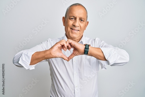 Handsome senior man wearing casual white shirt smiling in love doing heart symbol shape with hands. romantic concept.
