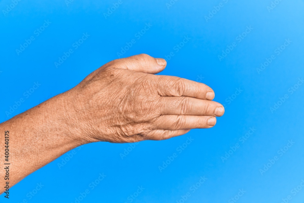 Hand of senior hispanic man over blue isolated background stretching and reaching with open hand for handshake, showing back of the hand Hand of senior hispanic man over blue isolated background stretching and reaching with open hand for handshake, showing back of the hand