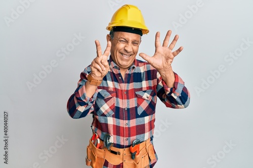 Senior hispanic man wearing handyman uniform showing and pointing up with fingers number seven while smiling confident and happy.