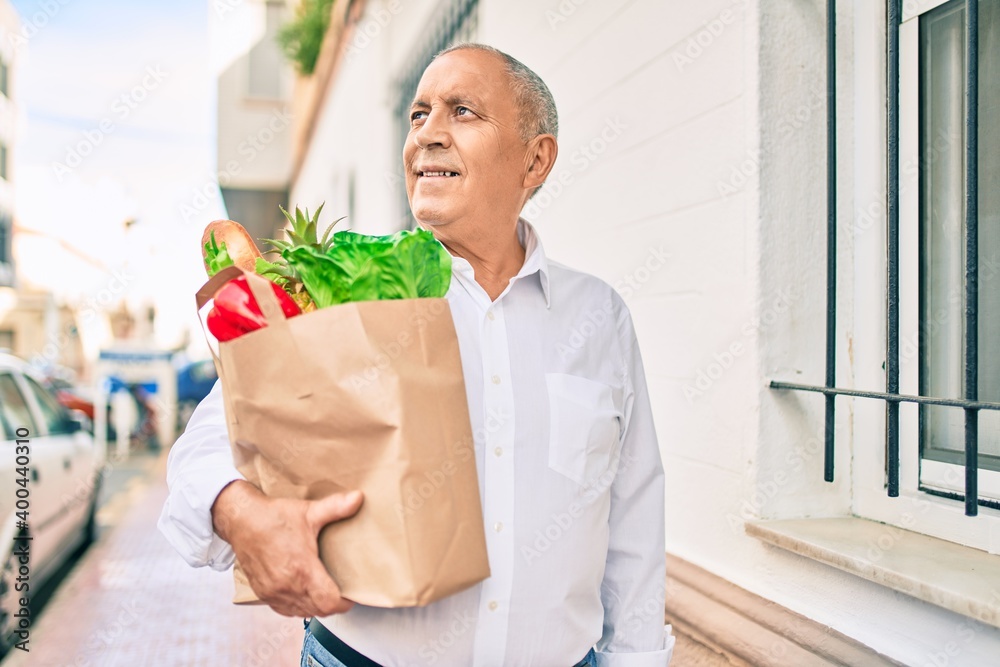 Senior man smiling happy holding paper bag with food walking at the city. Senior man smiling happy holding paper bag with food walking at the city.