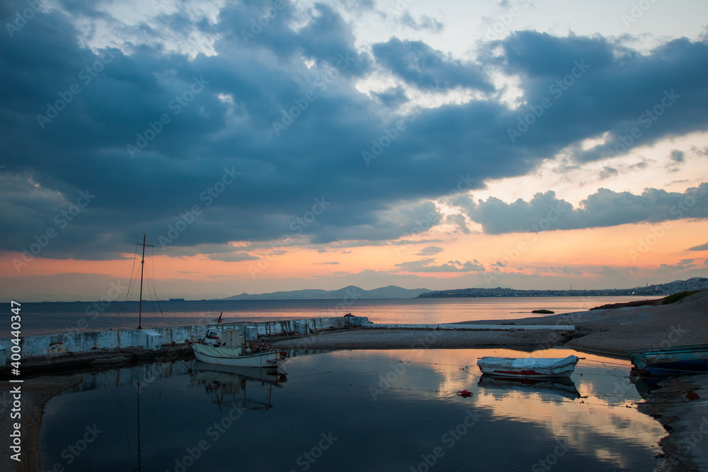 Fototapeta premium Sunset view of small fishing boats moored on Athens pier with reflections of cloudy sky in the water. Greece.