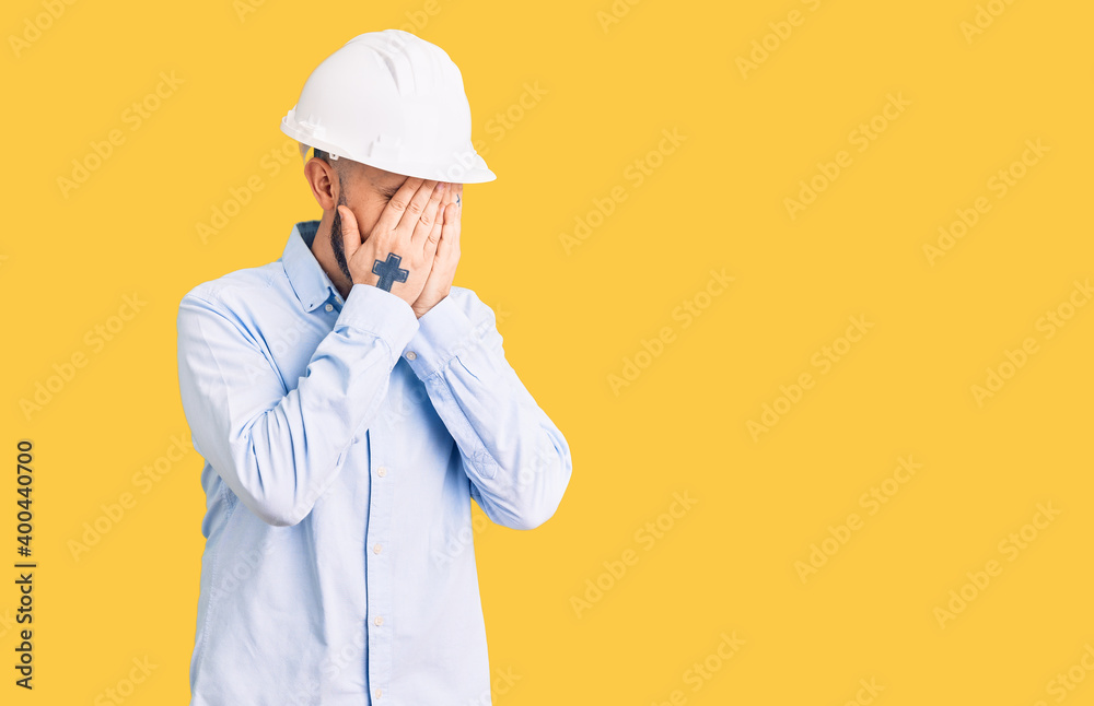 Young handsome man wearing architect hardhat with sad expression covering face with hands while crying. depression concept. Young handsome man wearing architect hardhat with sad expression covering face with hands while crying. depression concept.