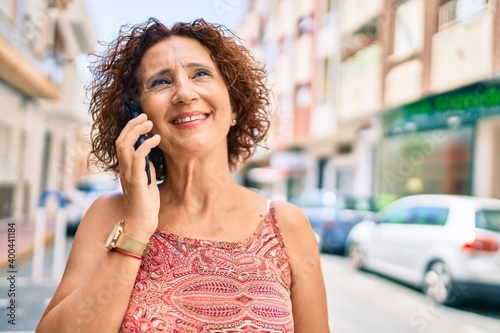 Middle age woman smiling happy talking on the smartphone walking at street of city.