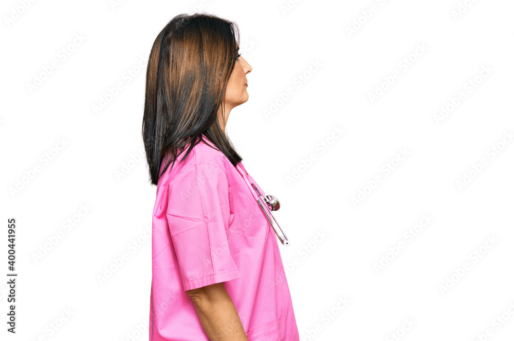 Middle age brunette woman wearing doctor uniform and stethoscope looking to side, relax profile pose with natural face with confident smile. Middle age brunette woman wearing doctor uniform and stethoscope looking to side, relax profile pose with natural face with confident smile.
