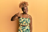Young african woman with afro hair wearing summer dress doing happy thumbs up gesture with hand. approving expression looking at the camera showing success.