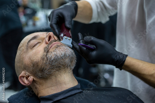 Close up portrait of a bearded man in barber shop during mustache trimming