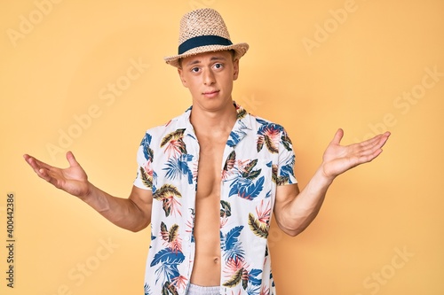 Young hispanic boy wearing summer hat clueless and confused with open arms, no idea and doubtful face.