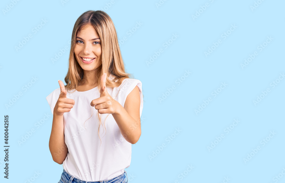 Beautiful caucasian woman with blonde hair wearing casual white tshirt pointing fingers to camera with happy and funny face. good energy and vibes.