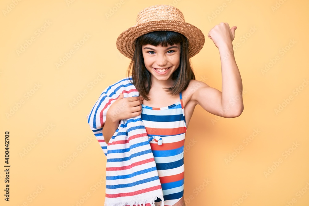 Young little girl with bang wearing swimsuit and summer hat holding towel screaming proud, celebrating victory and success very excited with raised arms Young little girl with bang wearing swimsuit and summer hat holding towel screaming proud, celebrating victory and success very excited with raised arms