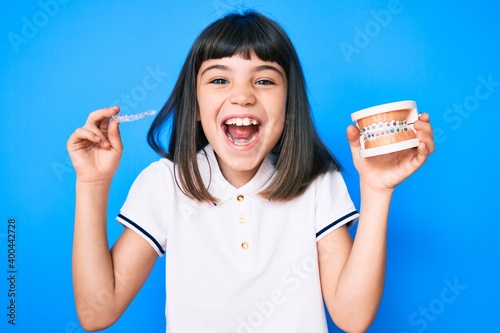 Young little girl with bang holding invisible aligner orthodontic and braces smiling and laughing hard out loud because funny crazy joke. photo