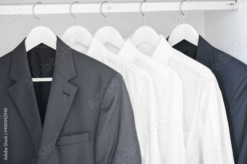 Men's modern white shirts and suits hanging on rack in wardrobe for businessman. 