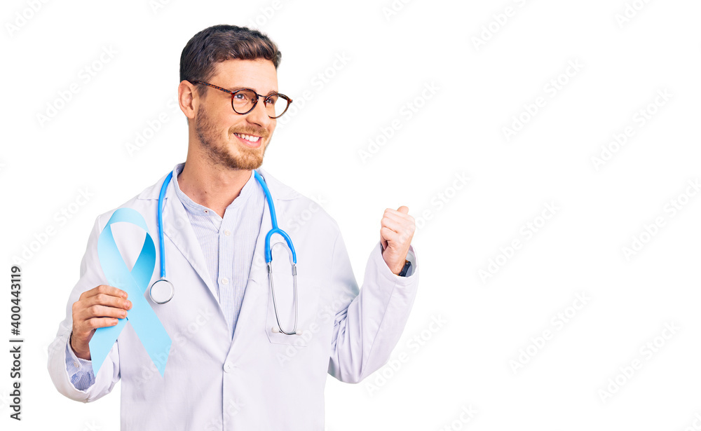 Handsome young man with bear wearing doctor uniform and holding blue ribbon pointing thumb up to the side smiling happy with open mouth Handsome young man with bear wearing doctor uniform and holding blue ribbon pointing thumb up to the side smiling happy with open mouth