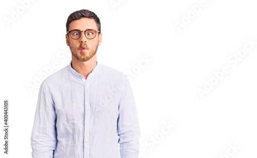 Handsome young man with bear wearing elegant business shirt and glasses making fish face with lips, crazy and comical gesture. funny expression.