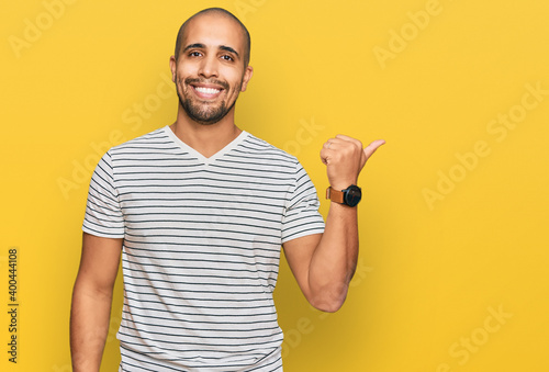 Hispanic adult man wearing casual clothes smiling with happy face looking and pointing to the side with thumb up.