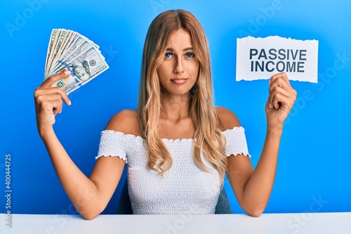 Foto Beautiful blonde young woman holding dollars and passive income text relaxed with serious expression on face