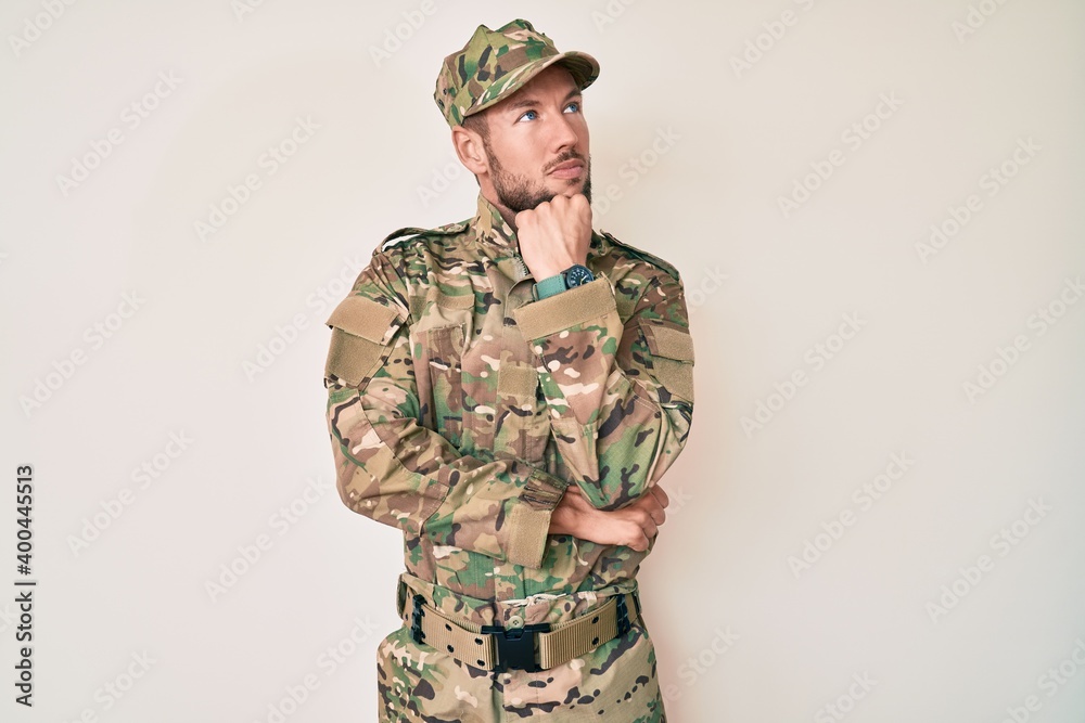 Young caucasian man wearing camouflage army uniform with hand on chin thinking about question, pensive expression. smiling with thoughtful face. doubt concept.