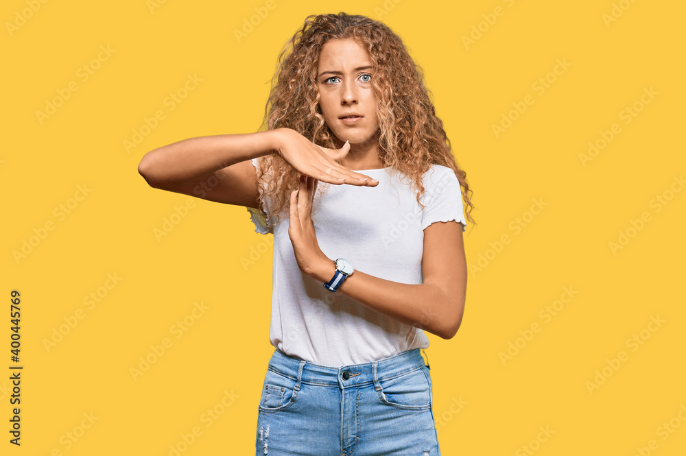 Beautiful caucasian teenager girl wearing casual white tshirt doing time out gesture with hands, frustrated and serious face