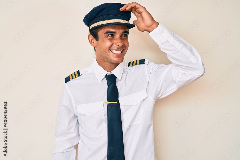 Young hispanic man wearing airplane pilot uniform smiling confident touching hair with hand up gesture, posing attractive and fashionable Young hispanic man wearing airplane pilot uniform smiling confident touching hair with hand up gesture, posing attractive and fashionable