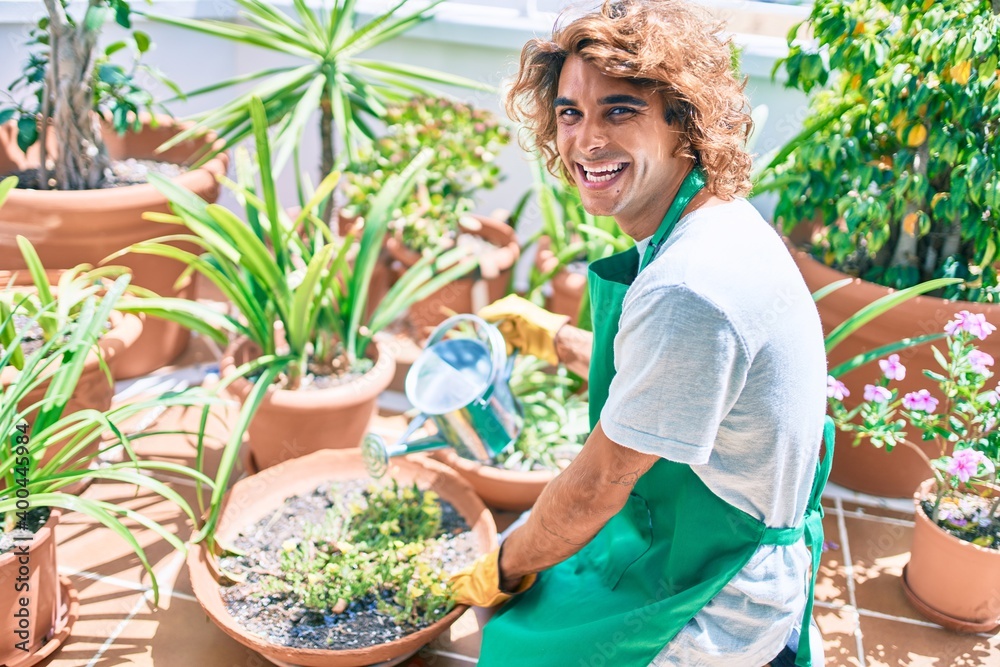 Young hispanic gardener smiling happy caring plants using watering can at terrace Young hispanic gardener smiling happy caring plants using watering can at terrace