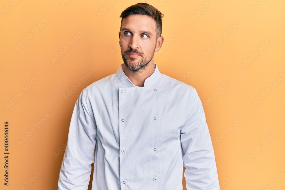 Handsome man with beard wearing professional cook uniform smiling looking to the side and staring away thinking. Handsome man with beard wearing professional cook uniform smiling looking to the side and staring away thinking.
