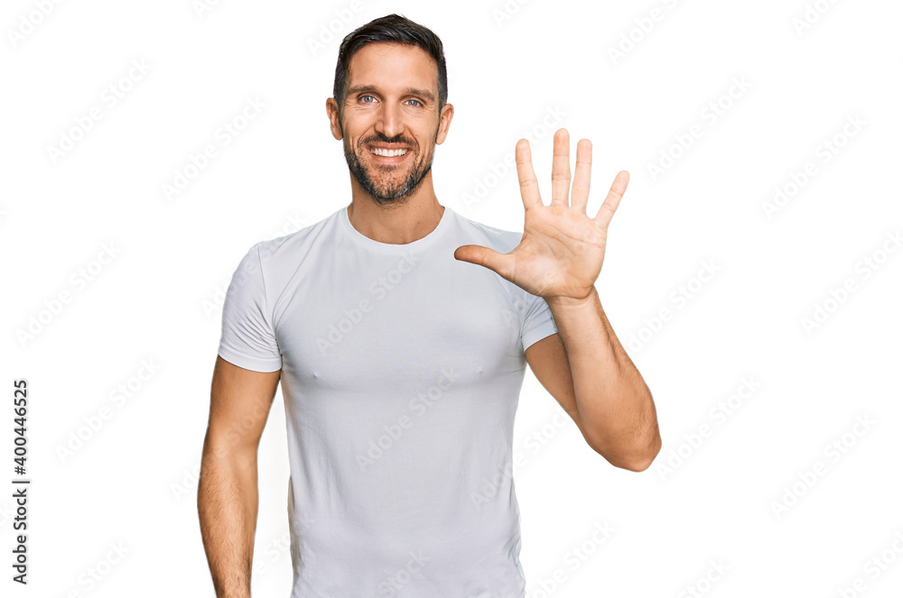 Naklejka premium Handsome man with beard wearing casual white t shirt showing and pointing up with fingers number five while smiling confident and happy.