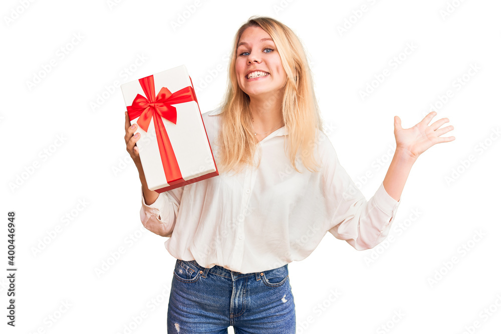 Young beautiful blonde woman holding gift annoyed and frustrated shouting with anger, yelling crazy with anger and hand raised Young beautiful blonde woman holding gift annoyed and frustrated shouting with anger, yelling crazy with anger and hand raised