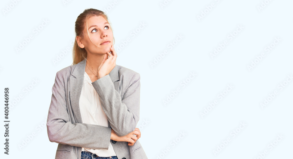 Young beautiful blonde woman wearing elegant jacket with hand on chin thinking about question, pensive expression. smiling with thoughtful face. doubt concept. Young beautiful blonde woman wearing elegant jacket with hand on chin thinking about question, pensive expression. smiling with thoughtful face. doubt concept.