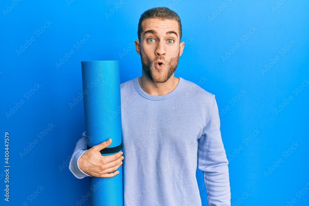Young caucasian man holding yoga mat scared and amazed with open mouth for surprise, disbelief face Young caucasian man holding yoga mat scared and amazed with open mouth for surprise, disbelief face