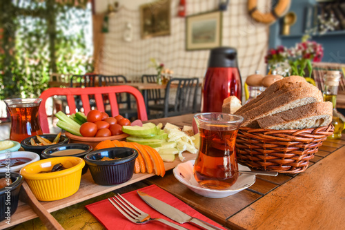Delicious rich Traditional Turkish breakfast include fruits, tomatoes, cucumbers, cheese plate (served with walnuts and dried fruits), butters, different kind of jam, honey, bread, olives and tea cup.