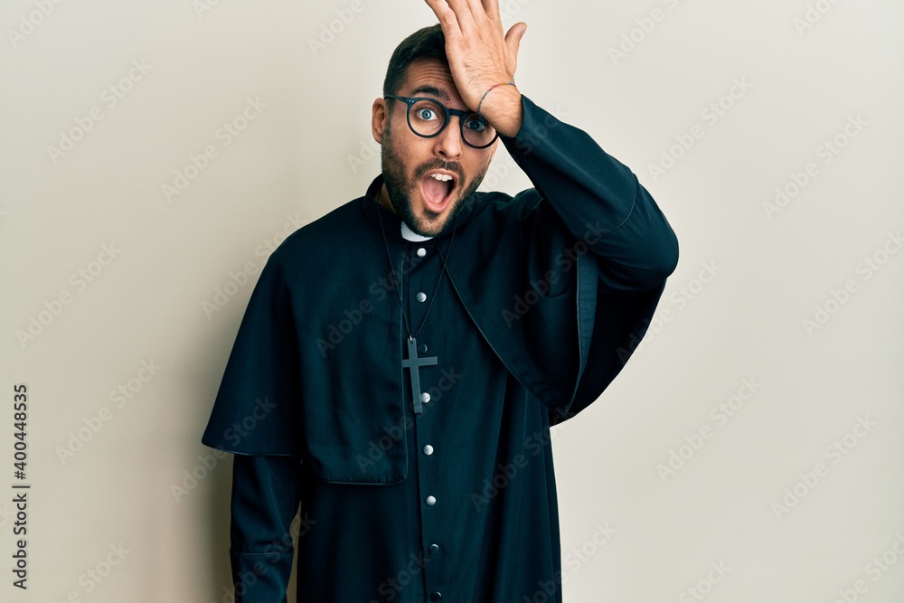 Young hispanic man wearing priest uniform standing over white background surprised with hand on head for mistake, remember error. forgot, bad memory concept.