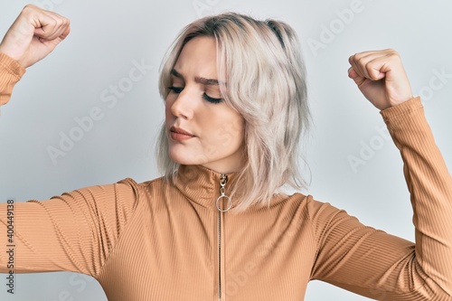 Young blonde girl wearing casual clothes showing arms muscles smiling proud. fitness concept.