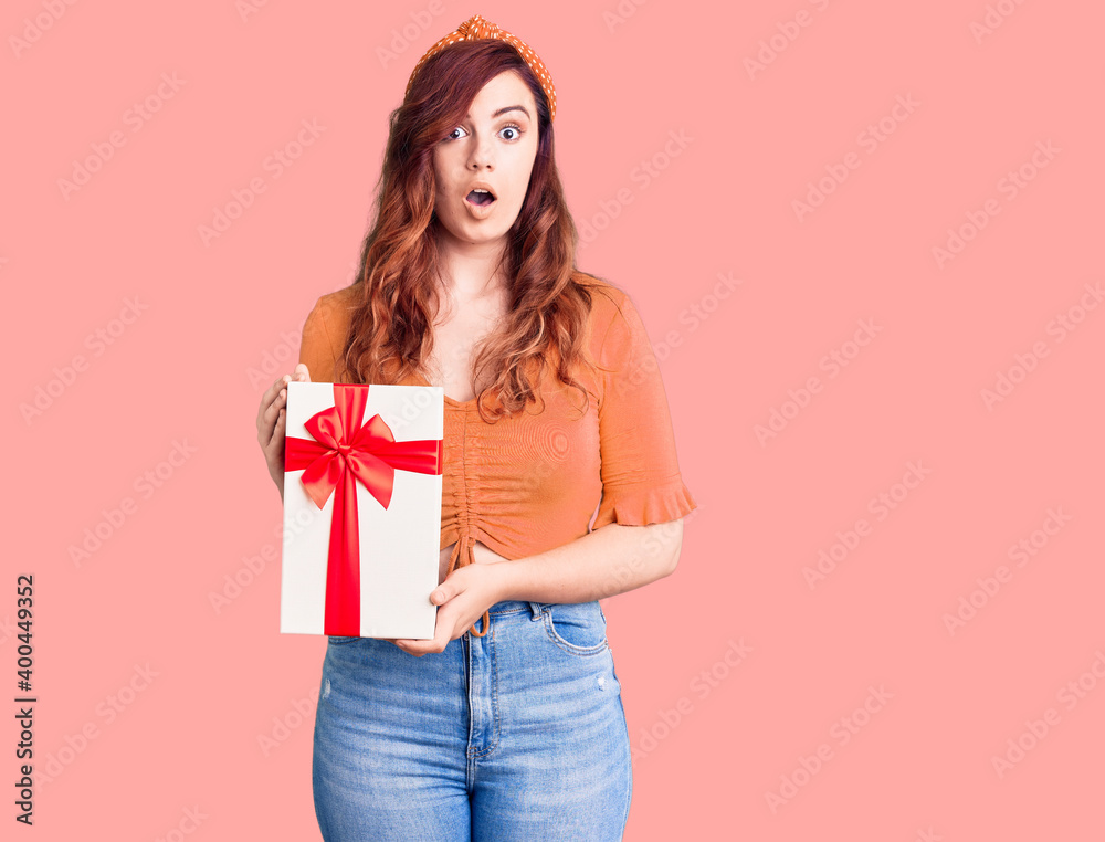 Young beautiful woman holding gift scared and amazed with open mouth for surprise, disbelief face