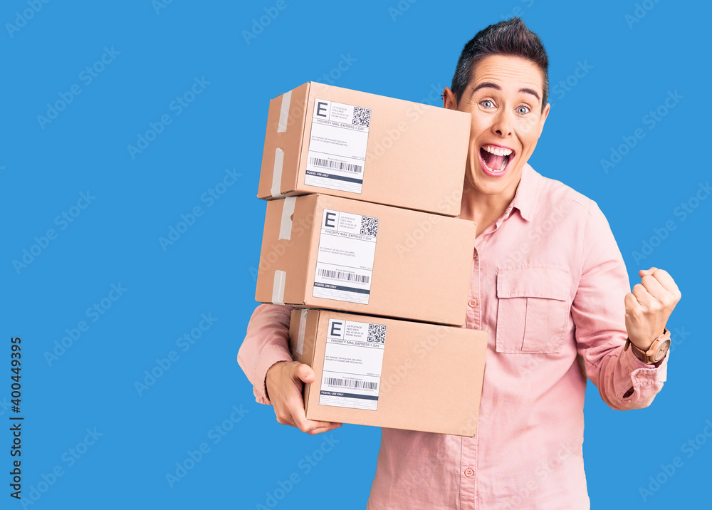 Young woman with short hair holding delivery package screaming proud, celebrating victory and success very excited with raised arms Young woman with short hair holding delivery package screaming proud, celebrating victory and success very excited with raised arms