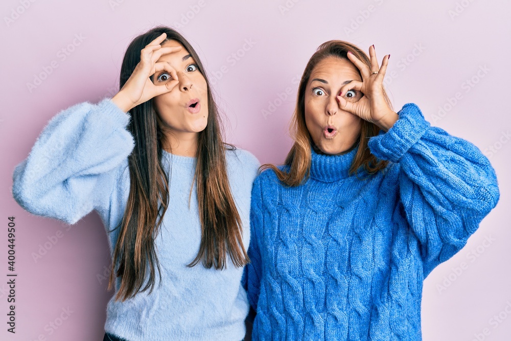 Hispanic family of mother and daughter wearing wool winter sweater doing ok gesture shocked with surprised face, eye looking through fingers. unbelieving expression. Hispanic family of mother and daughter wearing wool winter sweater doing ok gesture shocked with surprised face, eye looking through fingers. unbelieving expression.