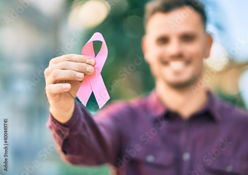 Young hispanic man smiling happy holding pink breast cancer ribbon at the city.