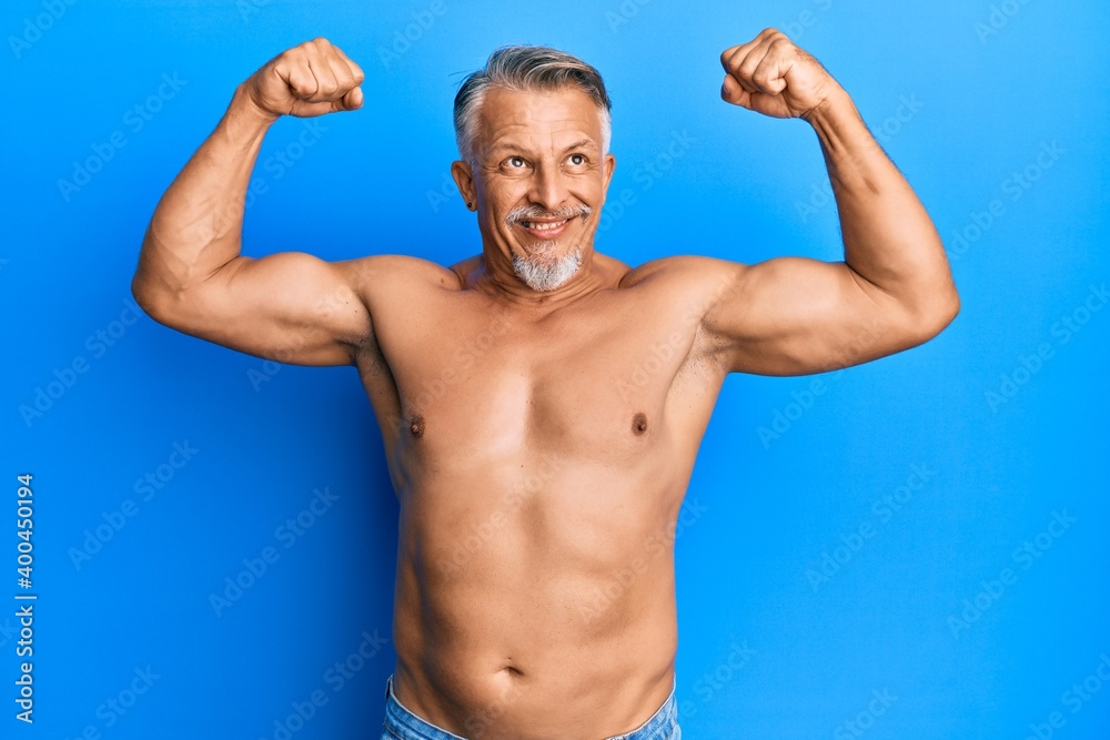 Middle age grey-haired man standing shirtless doing fitness gesture smiling looking to the side and staring away thinking.