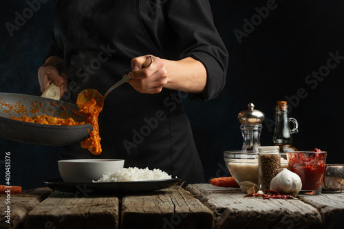 Professional chef pours traditional Indian chicken curry into bowl on dark blue background. Frozen motion. Concept cooking process. Frozen motion.