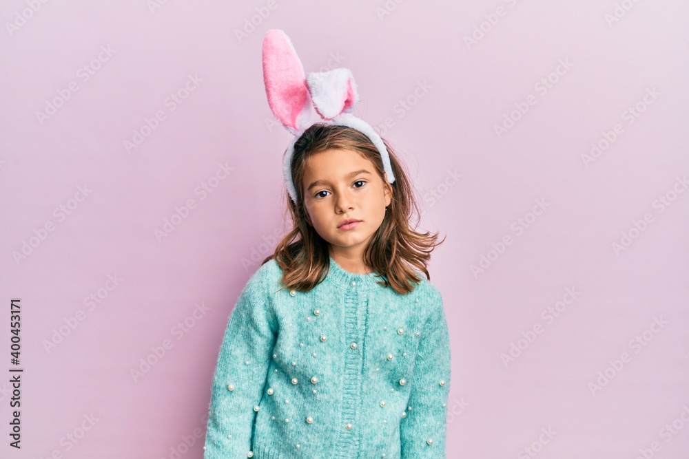 Little beautiful girl wearing cute easter bunny ears relaxed with serious expression on face. simple and natural looking at the camera.