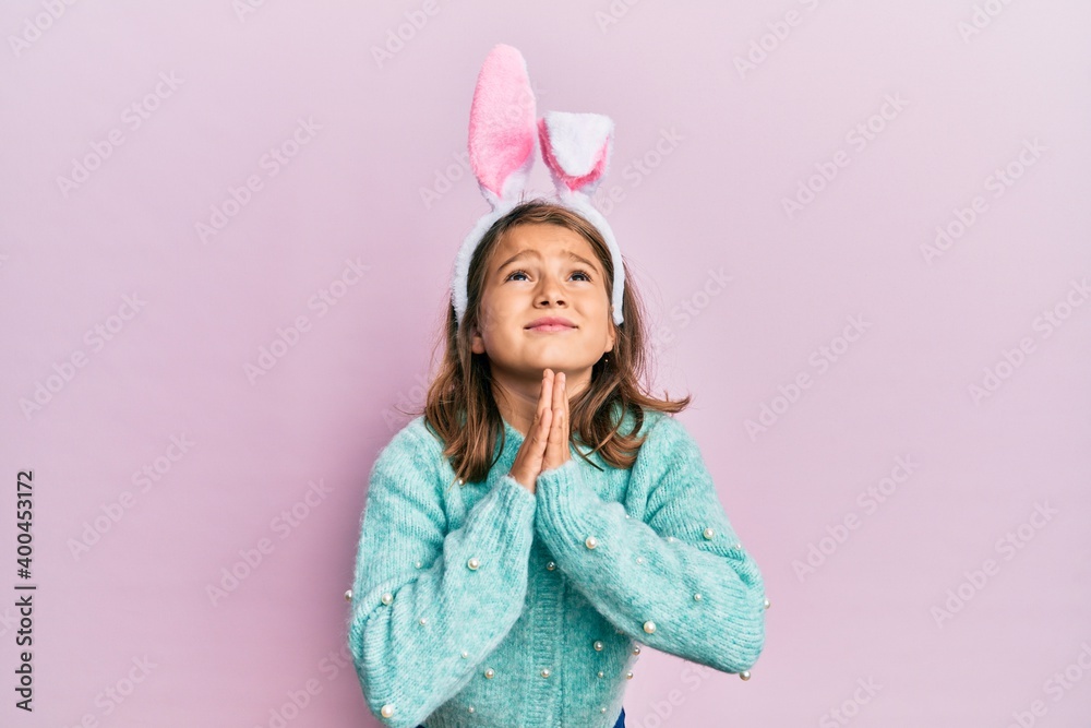 Little beautiful girl wearing cute easter bunny ears begging and praying with hands together with hope expression on face very emotional and worried. begging. Little beautiful girl wearing cute easter bunny ears begging and praying with hands together with hope expression on face very emotional and worried. begging.