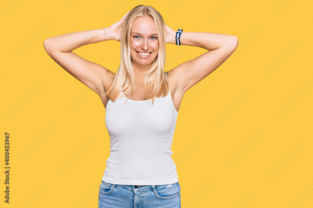 Young blonde girl wearing casual style with sleeveless shirt relaxing and stretching, arms and hands behind head and neck smiling happy Young blonde girl wearing casual style with sleeveless shirt relaxing and stretching, arms and hands behind head and neck smiling happy
