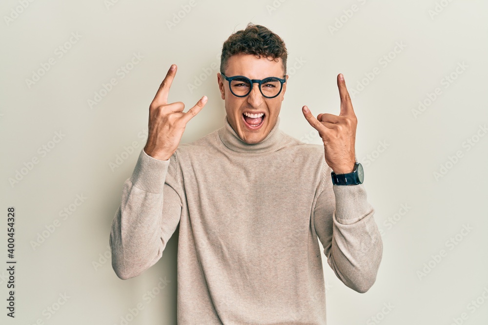 Fototapeta premium Hispanic young man wearing casual turtleneck sweater shouting with crazy expression doing rock symbol with hands up. music star. heavy music concept.