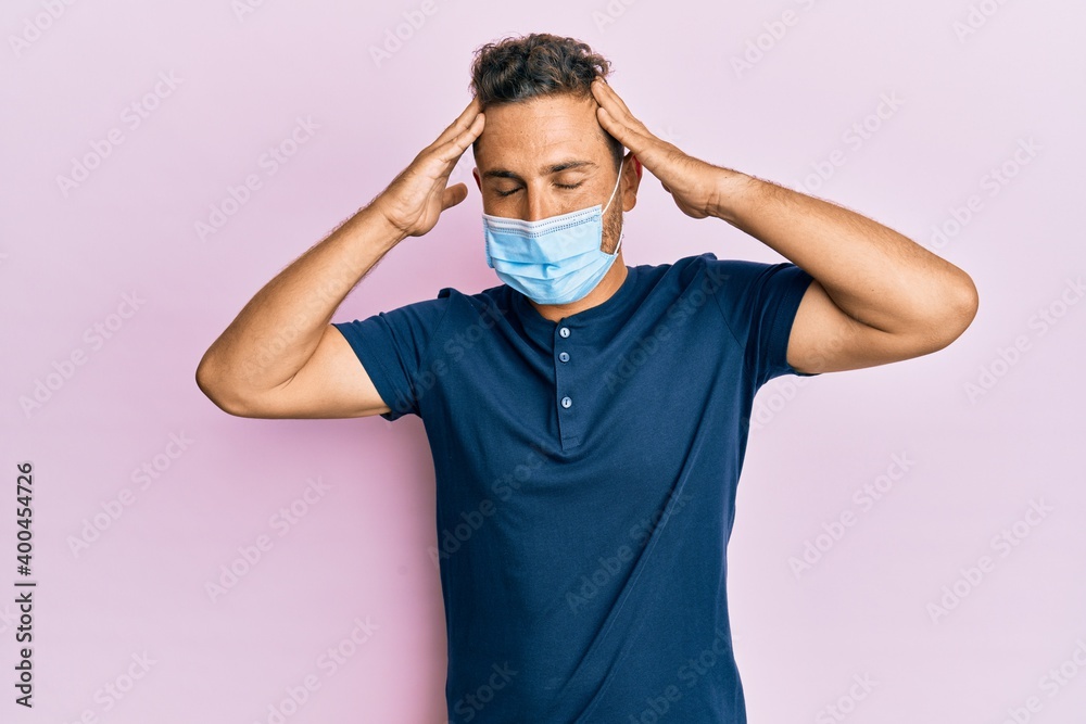 Handsome man with beard wearing medical mask with hand on head, headache because stress. suffering migraine. Handsome man with beard wearing medical mask with hand on head, headache because stress. suffering migraine.