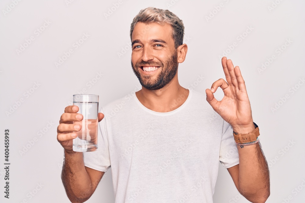 Handsome blond man with beard drinking glass of water to refreshment over white background doing ok sign with fingers, smiling friendly gesturing excellent symbol Handsome blond man with beard drinking glass of water to refreshment over white background doing ok sign with fingers, smiling friendly gesturing excellent symbol